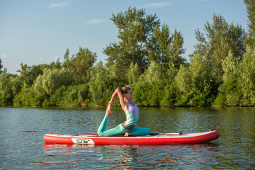 Fototapeta na wymiar Young woman doing yoga on sup board with paddle. Meditative pose, side view - concept of harmony with the nature