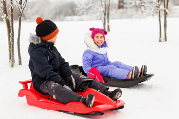 childhood, sledging and season concept - happy little kids sliding on sleds in winter