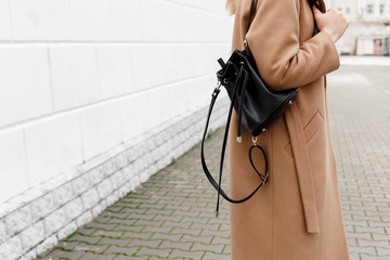 Woman in beige coat holding black backpack. Trendy stylish casual outfit. Details of everyday autumn, winter or spring look. Street fashion.