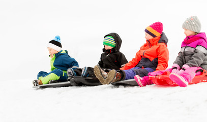 Fototapeta na wymiar childhood, sledging and season concept - group of happy little kids sliding on sleds in winter