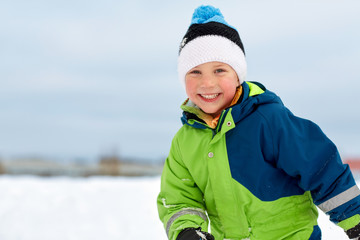 childhood, leisure and season concept - happy little boy in winter clothes outdoors