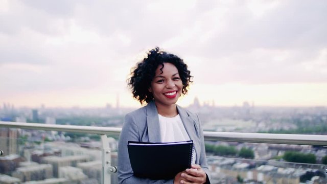 A portrait of a businesswoman standing on a terrace, holding notes.