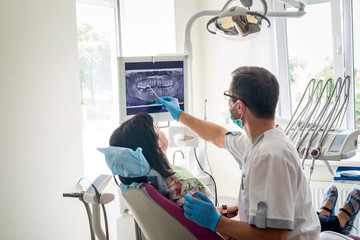 Doctor dentist showing patient's teeth on X-ray - obrazy, fototapety, plakaty
