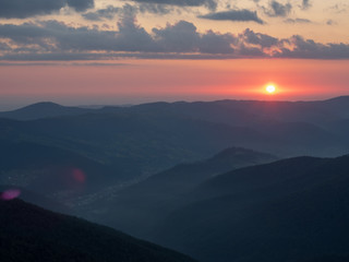 Landscape of red sunset in mountains. The sun illuminating horizon with red light. Clouds flowing in the sky above dark peaks. Carpathians mountains at summer, west Ukraine. Blurred background