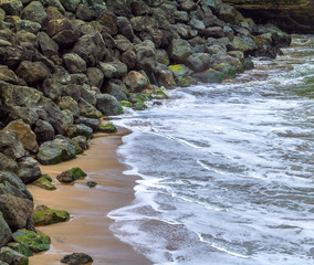 Ocean tide aganist rocks and sand on the shore.