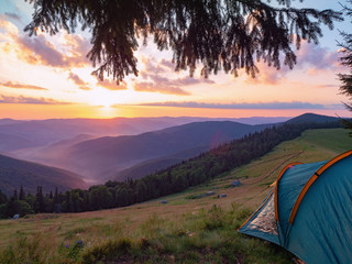 Obraz premium Sunset in Carpathians mountains at summer, Ukraine. Touristic tent on mountain meadow. The sun illuminating clouds and mountains peaks. Ukrainian nature landscape in august. Blurred background