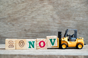 Toy forklift hold block V to complete word 20nov on wood background (Concept for calendar date 20 in month November)