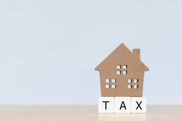Obraz na płótnie Canvas House model and wooden cubes with alphabet TAX on wooden table. Home taxes decrease concept