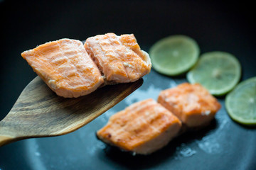 Close up grilled salmon steak on black pan with 3 lemon slices. image for background, wallpaper and copy space.