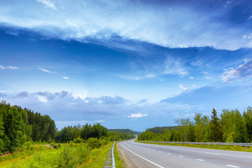 asphalt road through the forest with clouds, summer