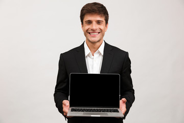 Businessman standing isolated holding laptop computer showing empty display.
