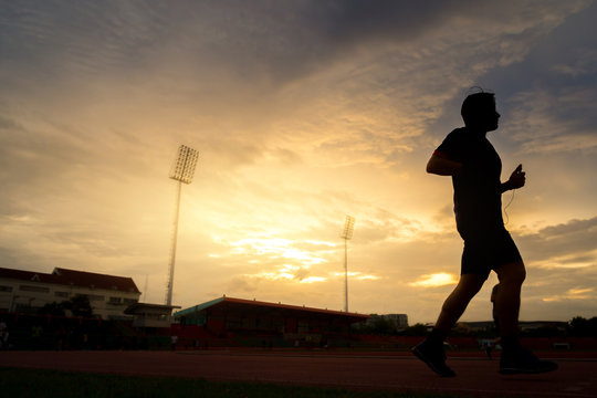Young people runs at the stadium on beautiful sunset. Silhouette picture of runners on sunset background, wellness concept.