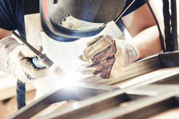 Male in face mask welds with argon-arc welding