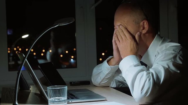 Executive businessman rubbing eyes while hard work by notebook in night office