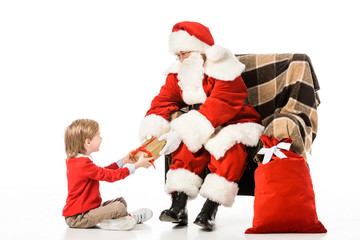 santa presenting christmas gift to kid while sitting in armchair isolated on white