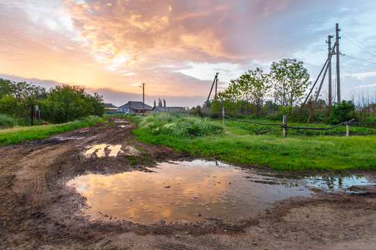 The spring in the russian village. The landscape with the mud road, the puddle and beautiful sunrise sky