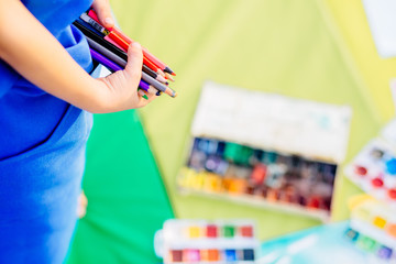 Cute little girl in blue apron drawing with colorful pensils in summer park. Creative child painting on nature. Outdoors activity for children. Talented painter. Close up of hands.