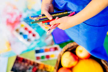 Close up of hands little girl in blue apron drawing still life with colorful pensils in summer park. Creative child painting on nature. Outdoors activity for children. Talented painter.