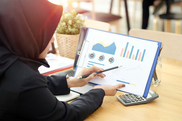 Attractive young Asian wearing dark hijab showing data on paperwork.
