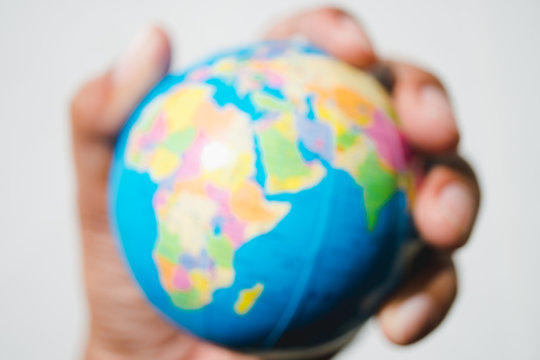 Abstract blurred hand holding small earth on grey background