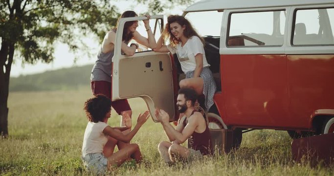 Group of friends have a good time together in the middle of nature playing with hands , standing up beside of a retro bus.