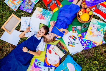 Authentic artist children in blue aprons girl and boy paints lying in creative chaos palette watercolor paints palette and brush . Painting outdoor grass autumn.Top view handmade crafts.