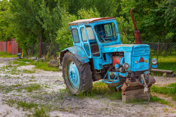The old blue tractor without front wheels in the russian village