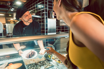 Experienced chef choosing raw seafood from the freezer for two customers in a trendy restaurant or...