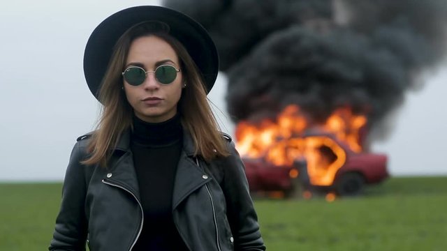 Girl musician on the background of a burning car, a stern look, a girl in black, a car explosion