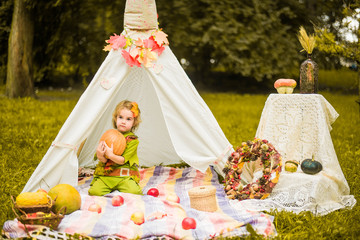 Little girl lying and playing in a tent, children's house wigwam in park Autumn portrait of cute curly girl. Harvest or Thanksgiving. autumn decor, party, picnic. Child in halloween costume. © MartaKlos
