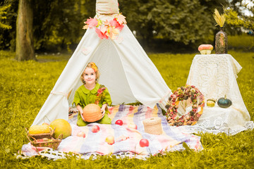 Little girl lying and playing in a tent, children's house wigwam in park Autumn portrait of cute curly girl. Harvest or Thanksgiving. autumn decor, party, picnic. Child in halloween costume. © MartaKlos