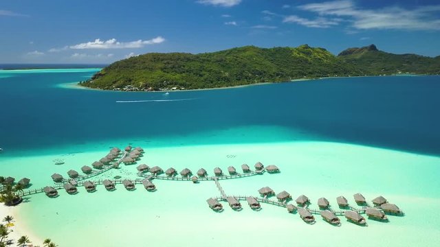 Aerial footage from a drone of luxury overwater villas with palm trees, blue lagoon, white sandy beach and Otemanu mountain at Bora Bora island, Tahiti, French Polynesia (Bora Bora Aerial)
