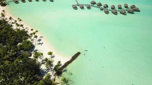 Aerial footage from a drone of luxury overwater villas with palm trees, blue lagoon, white sandy beach and Otemanu mountain at Bora Bora island, Tahiti, French Polynesia (Bora Bora Aerial)
