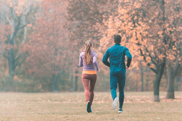 Fall running in a park, seen from behind couple of man and woman 
