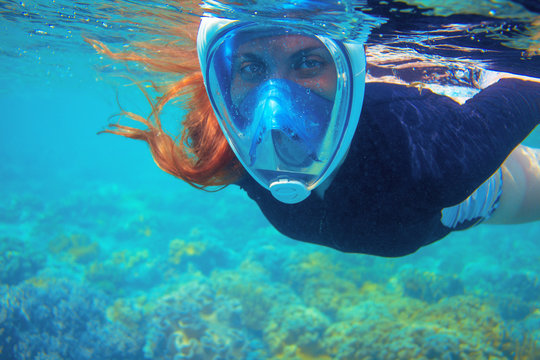Red hair snorkeling girl full-face snorkeling mask in coral reef. Snorkel in coral reef of tropical sea.