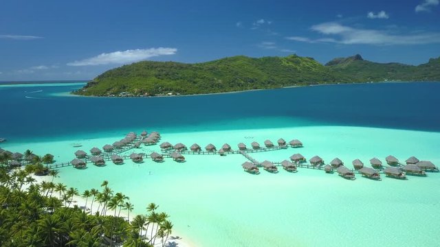 Aerial footage from a drone of luxury overwater villas with palm trees, blue lagoon, white sandy beach and Otemanu mountain at Bora Bora island, Tahiti, French Polynesia (Bora Bora Aerial)
