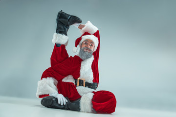 Funny serious guy with christmas hat dancing at studio. New Year Holiday. Christmas, x-mas, winter, gifts concept. Man wearing Santa Claus costume on gray. Copy space. Winter sales.