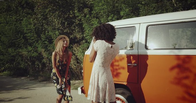 Two pretty girls making photo shoot on the road beside the vintage orange bus , happy dancing and smiling , wearing boho style clothes.