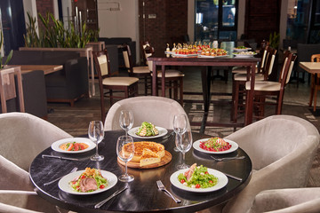 A solemn table with glasses and a variety of different dishes from the chief chef in the foreground. Buffet table with appetizers, canapes and sandwiches in the background.