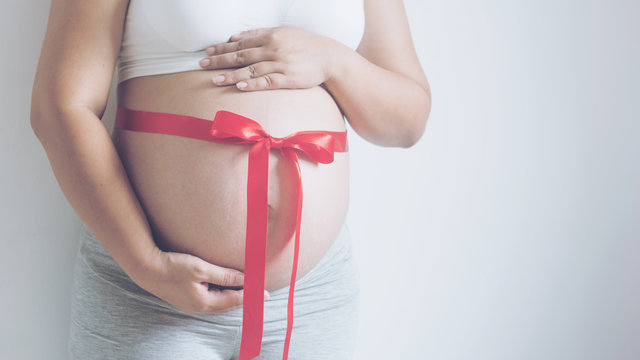 Close up image of pregnant woman tummy with red ribbon. - Powered by Adobe