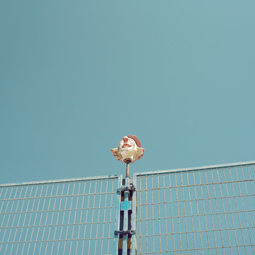 Imagen de cabeza de payaso coronando una verja de una cancha deportiva. Cielo azul despejado, escena diurna