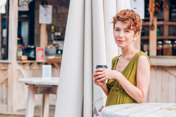 A beautiful woman in a summer cafe with coffee in her hands looks at the camera