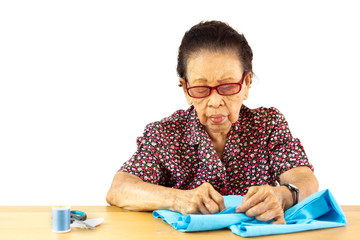 Elder Asian lady age between 80-85 years old is sewing a cloth professionally.  Isolated on white background.