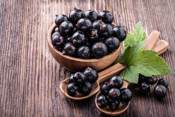 Fresh ripe black currant in wooden bowl with original leaves and two spoons on rustic old background.