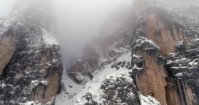 Backward aerial from snowy rocky mountain tilting down.Cloudy bad overcast foggy weather.Winter Dolomites Italian Alps mountains outdoor nature establisher.4k drone flight