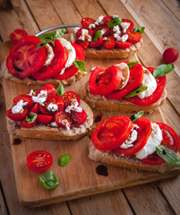 Bruschetta with cheese, tomatoes, fresh basil and balsamic vinegar on cutting board