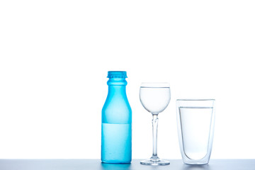 Image of a blue plastic bottle, wine glass and double glass filled with water close up, isolated on white background.