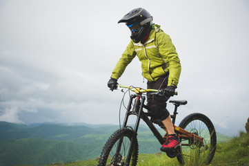 A man in a mountain helmet riding a mountain bike rides around the beautiful nature in cloudy weather. downhill