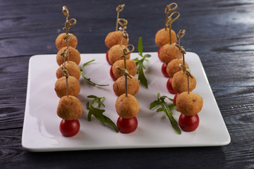 Appetizing and unusual snack for the festive table. A small treat on a skewer. A tiny round cutlet in breadcrumbs and a cherry tomato. Vegetarian snack with potato ball and tomato.