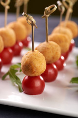 Appetizing and unusual snack for the festive table. A small treat on a skewer. A tiny round cutlet in breadcrumbs and a cherry tomato. Vegetarian snack with potato ball and tomato.